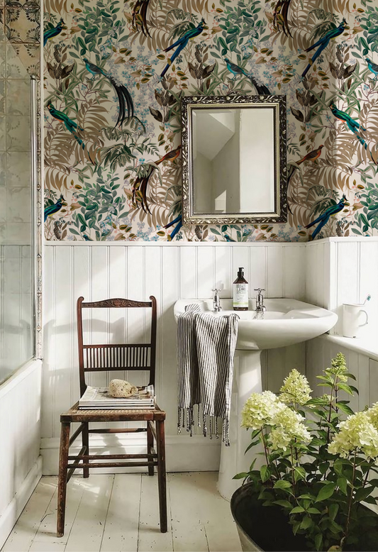 Vintage inspired bathroom with antique chair , sink and mirror surrounded by botanical Deus ex Gardenia's Resplendent Woods Wallpaper in Shaded White. Photo by Park Place Gower.